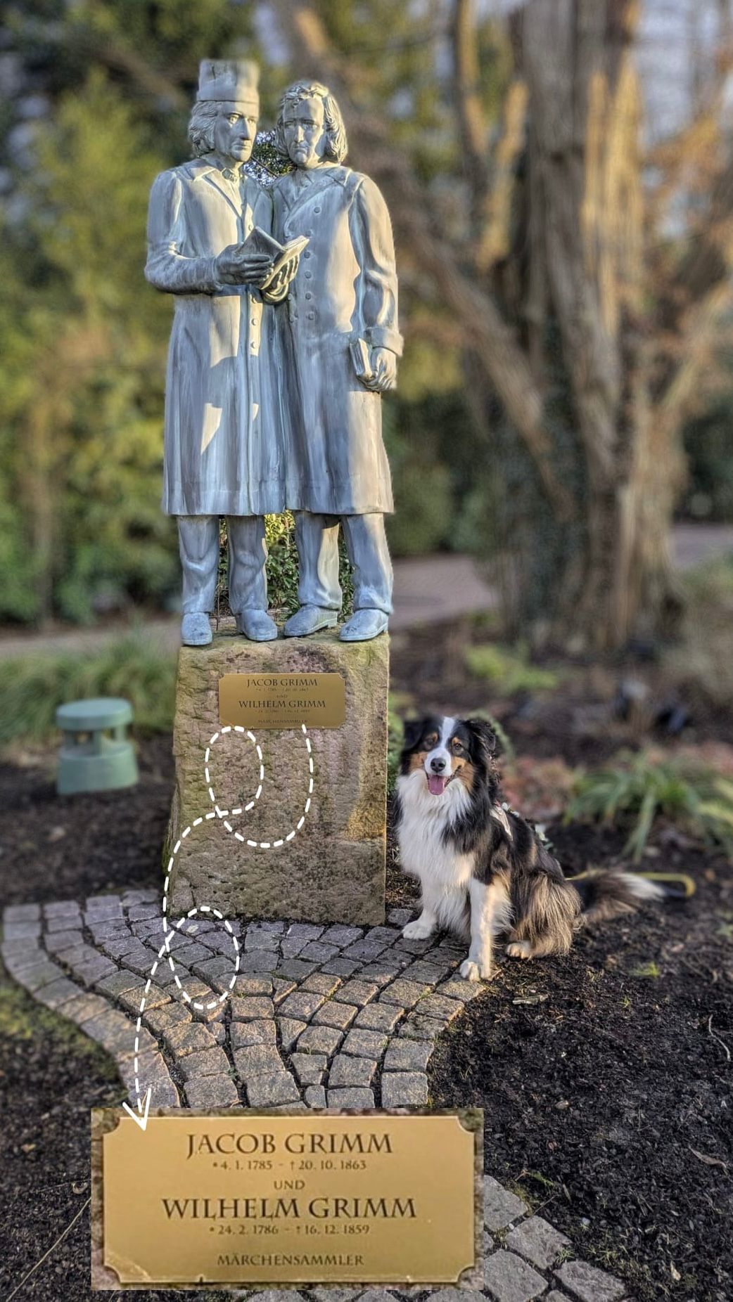 Ein Hund namens Grimm sitzt vor einer Statue der Gebrüder Grimm