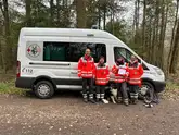 Rettungshundeteam mit Prüfern vor einem Einsatzfahrzeug
