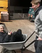 Eine Frau wird in einem Schubkarren geschoben auf dem Gelände eines Dachdeckers beim rettungshundetraining