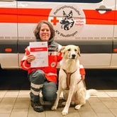 Larry und Mirka Rettungshundeteam nach der Prüfung mit der Urkunde vor einem Einsatzwagen