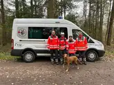 Rettungshundeteam mit Prüfern vor einem Einsatzfahrzeug