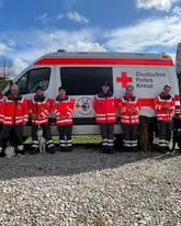 Rettungshundeteams mit Prüfern vor einem Einsatzfahrzeug