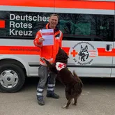 Rettungshundeteam mit Urkunde vor Einsatzwagen
