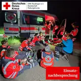 Titelbild Einstznachbesprechung 2025 Einsatzkräfte sitzen bei Nacht vor einem Einsatzfahrzeug auf dem Boden und Besprechen den Einsatz