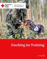Titelbild Faschin im Training 2026 Person mit Tarnanzug im Wald füttert Rettungshund mit Kenndecke