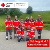 Titelbild Prüfung Grundgehorsam Einsatzkräfte des DRK der Rettungshunde zum Gruppenbild auf einem geteerten Platz vor einer Wiese