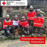 Einsatzkräfte der Rettungshunde des DRK sitzen mit einem Hund auf Trümmern nach einer erfolgreichen Prüfung in der Vermisstensuche